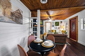 Uma área de refeições com uma mesa posta para dois, um ventilador de teto e uma porta vermelha ao fundo.