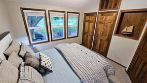 Un dormitorio con cama, almohadas, ventana y armario de madera.