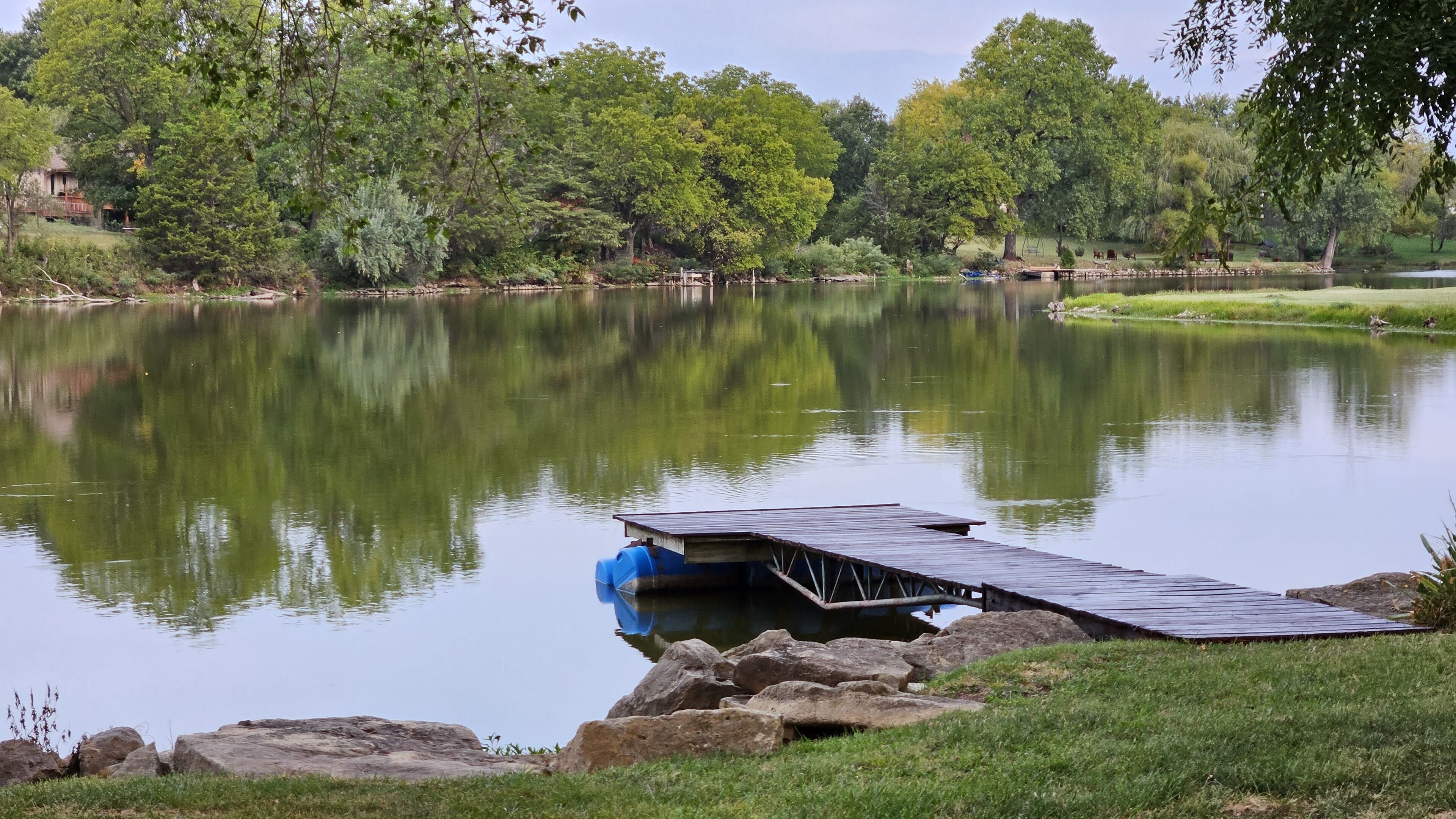 Um lago tranquilo com um cais que se estende sobre a água, cercado por vegetação exuberante e árvores.