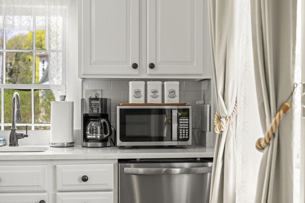A kitchen with white cabinets, a coffee maker, a microwave, and a dish rack.