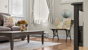 A living room with a wooden coffee table, a sofa with alphabet pillows, a floral vase, a chair with a map, and a globe on a stand. - Historic Waterfront School House (Groton)