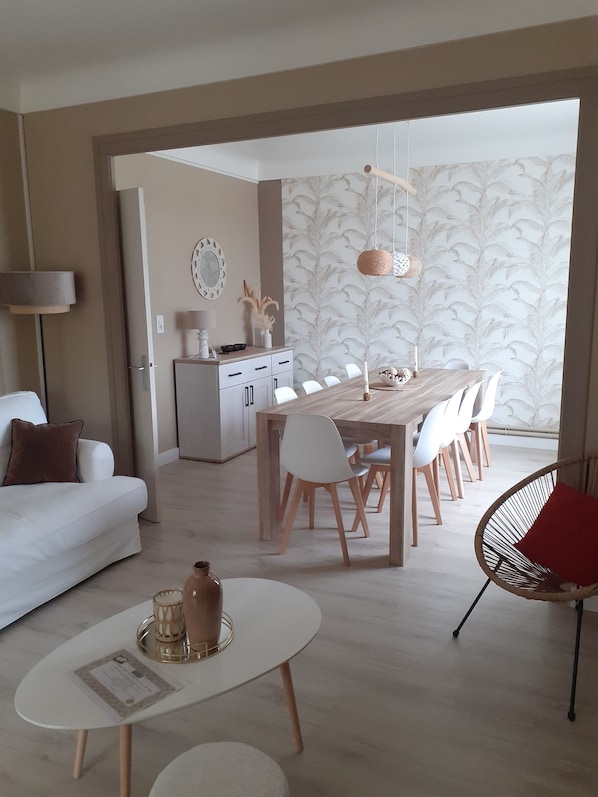 Un salon moderne avec un canapé blanc, une table basse ronde et un coin repas comprenant une table en bois et des chaises blanches.