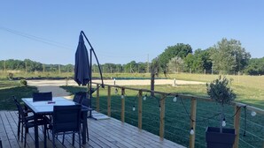 A wooden deck with a table and chairs, a trash bin, and a view of a grassy field and trees. - House with swimming pool 2 minutes from Lougratte lake, ideal for families. (Cancon)
