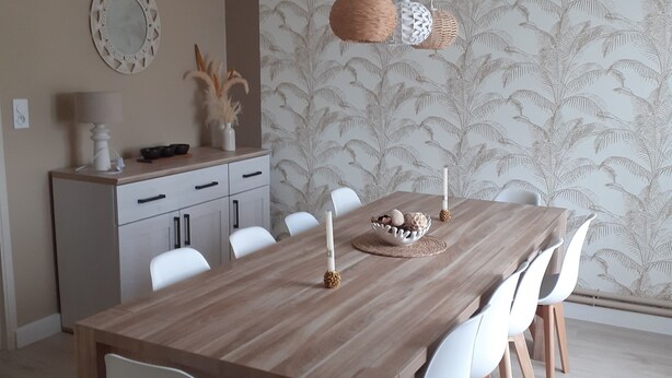 A dining area with a wooden table and white chairs, a hanging light fixture, and a decorative wall with a leaf pattern. - House with swimming pool 2 minutes from Lougratte lake, ideal for families. (Cancon)