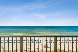 Una playa con hileras de sombrillas azules y sillas reclinables, una torre de salvavidas y una vista despejada del océano.