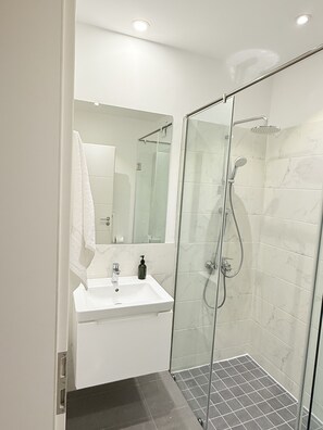 A modern bathroom with a glass-enclosed shower, a white sink, and a mirror above it.