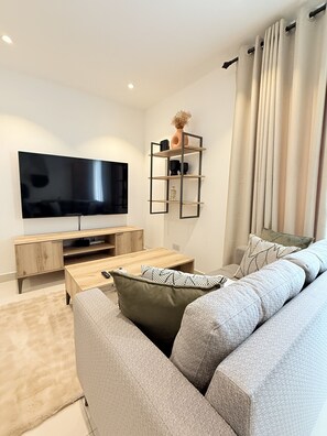 Una sala de estar moderna con un televisor de pantalla plana, muebles de madera, un sofá gris y una estantería decorativa.