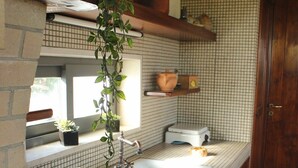 Una cocina con salpicadero de azulejos, armarios de madera, un lavamanos empotrado, un frutero y una planta colgante.