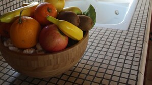 Una cocina con salpicadero de azulejos, un bol de frutas de madera en la encimera, una ventana con plantas en macetas y un lavabo.