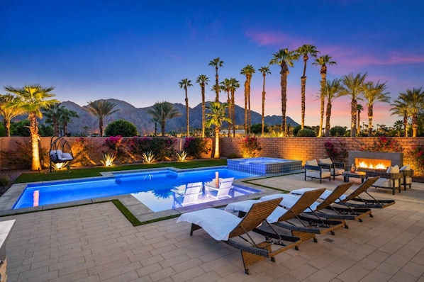 A pool area with lounge chairs, a hot tub, and a fire feature.