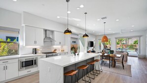 A modern kitchen with a large island, bar stools, and pendant lighting. - Desert mountain views w/ pool, fire pit & hot tub (La Quinta)