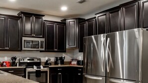 A modern kitchen with dark cabinets, stainless steel appliances, and a tiled floor. - Mickey's Mansion Luxury Themed Pool Home, Arcade, Theater (Four Corners)