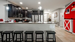 A modern kitchen with dark cabinets, stainless steel appliances, and a central island with bar stools. - Mickey's Mansion Luxury Themed Pool Home, Arcade, Theater (Four Corners)