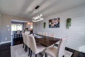A dining room with a dark wooden table, beige upholstered chairs, a hanging light fixture, and a floral painting on the wall. - 6BR Home w/ Pool - Spooky Nook/MiamiU/KingsIsland (Hamilton)