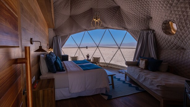Een knus, tentachtig interieur met een bed, bank en uitzicht op een woestijnlandschap.