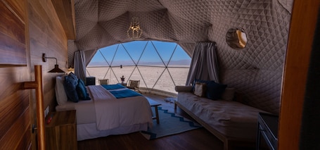 A cozy, tent-like interior with a bed, sofa, and a view of a desert landscape.