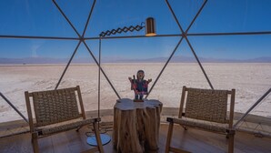 Een kamer met een centrale tafel, twee stoelen, een metalen frame en uitzicht op een woestijnlandschap.