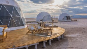 Een reeks koepelvormige jurten met houten terrassen en zitplaatsen, gelegen voor een bewolkte lucht en verre bergen.