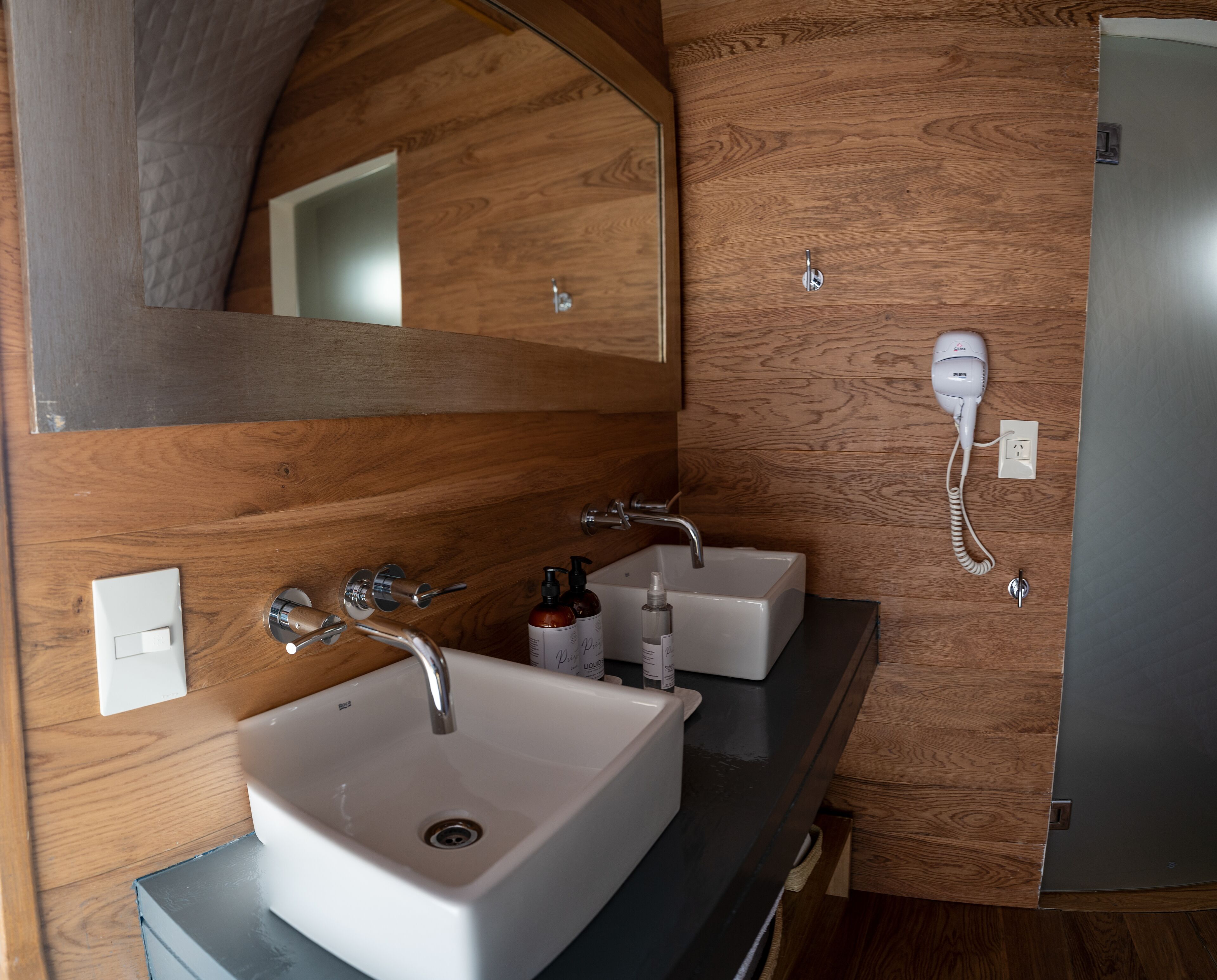 Un bagno con un lavandino bianco, due rubinetti, uno specchio e un asciugacapelli montato a parete.