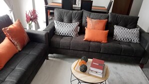 A living room with a dark grey sofa, orange and patterned cushions, a round coffee table with a book and decorative balls, and a patterned rug. - luxurious apartment 1 bedroom ,1 bathroom with many exciting amenities  (Accra)
