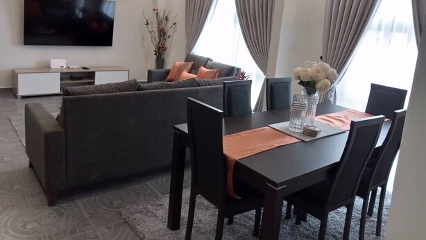 A modern living room with a sofa, dining table, chairs, a TV, and large windows with curtains. - luxurious apartment 1 bedroom ,1 bathroom with many exciting amenities  (Accra)