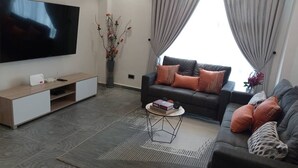 A modern living room with a flat-screen TV, a sofa, a coffee table, and a decorative vase. - luxurious apartment 1 bedroom ,1 bathroom with many exciting amenities  (Accra)