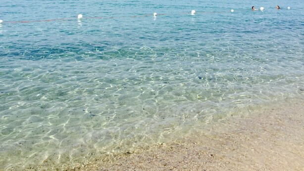 Una spiaggia limpida con acque calme e una barca in lontananza.