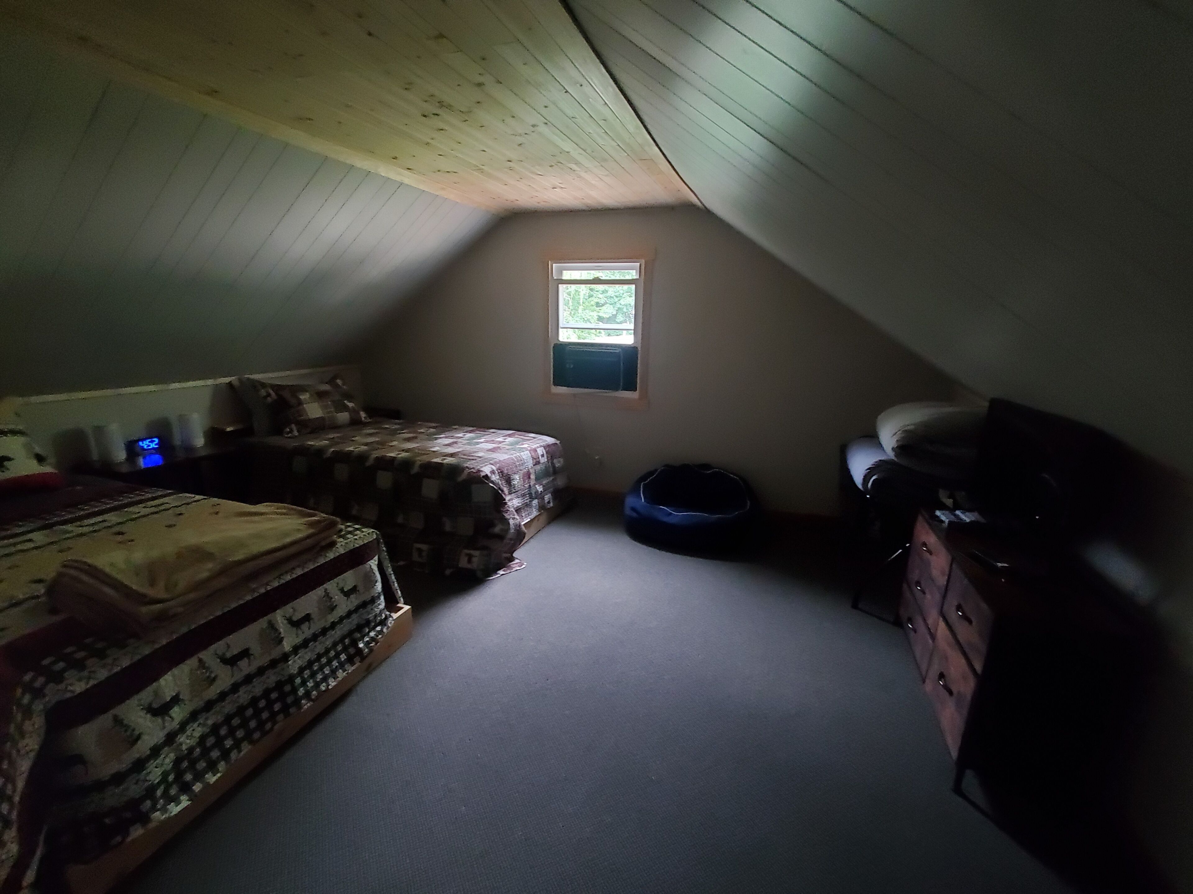 A small attic bedroom with a sloped ceiling, a single window, a bed, a dresser, and a small table.