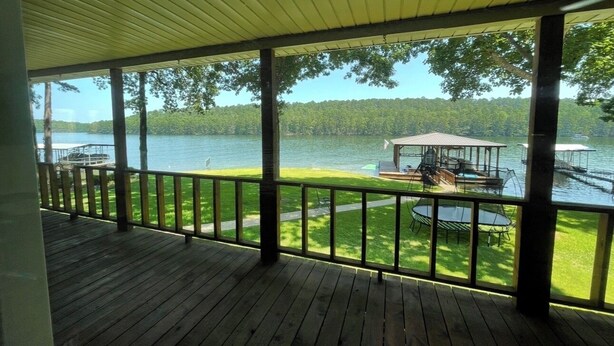 Une terrasse couverte avec une balustrade donnant sur un lac, un belvédère et un quai avec des bateaux.