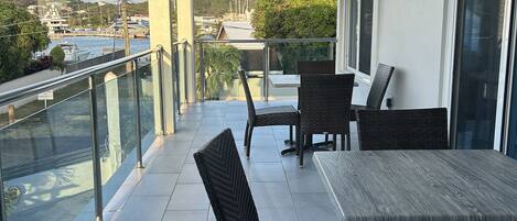 A balcony with a table and chairs, overlooking a marina and hills.