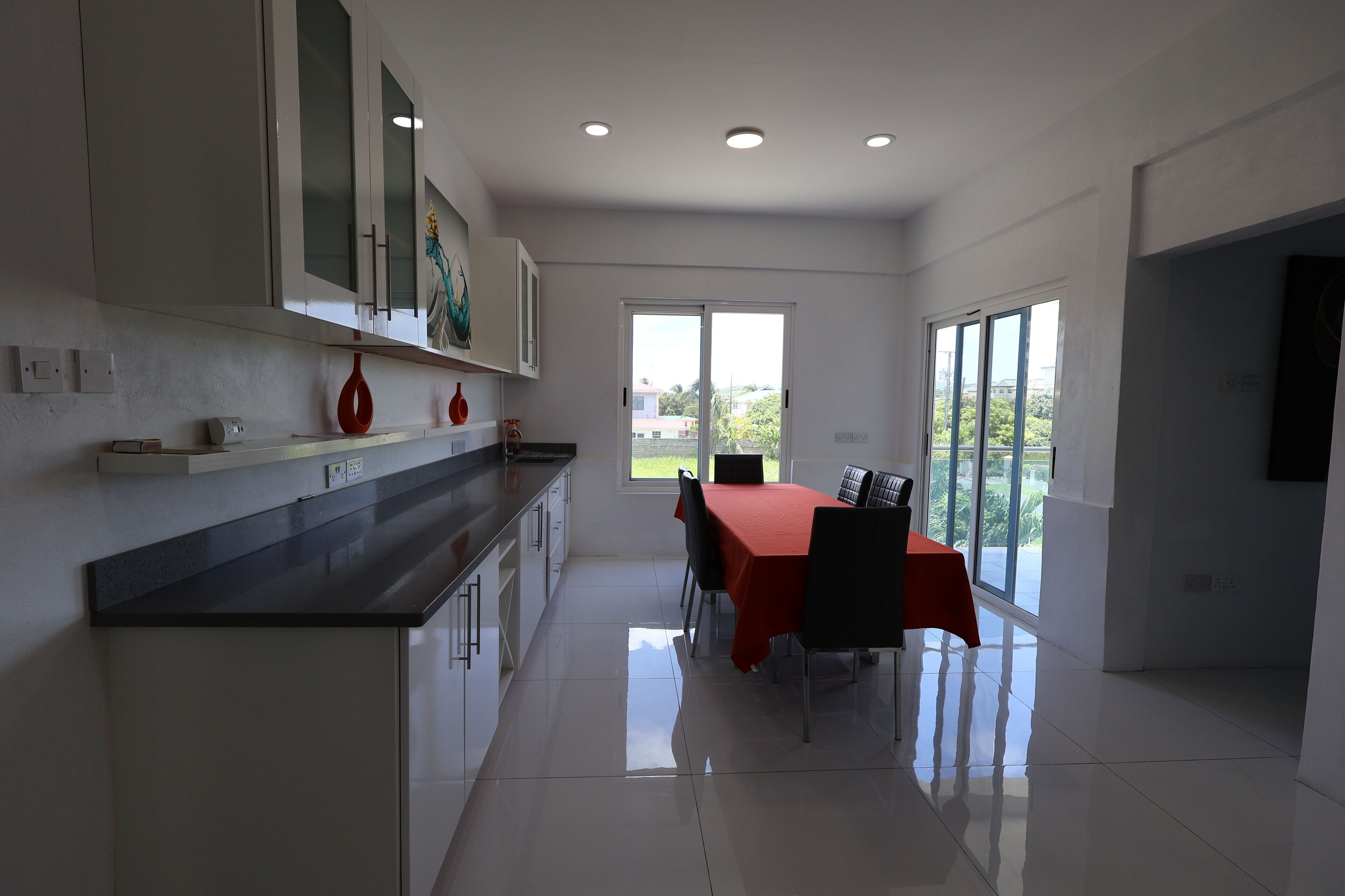 A modern kitchen with white cabinets, a black countertop, and a dining area with a red tablecloth.