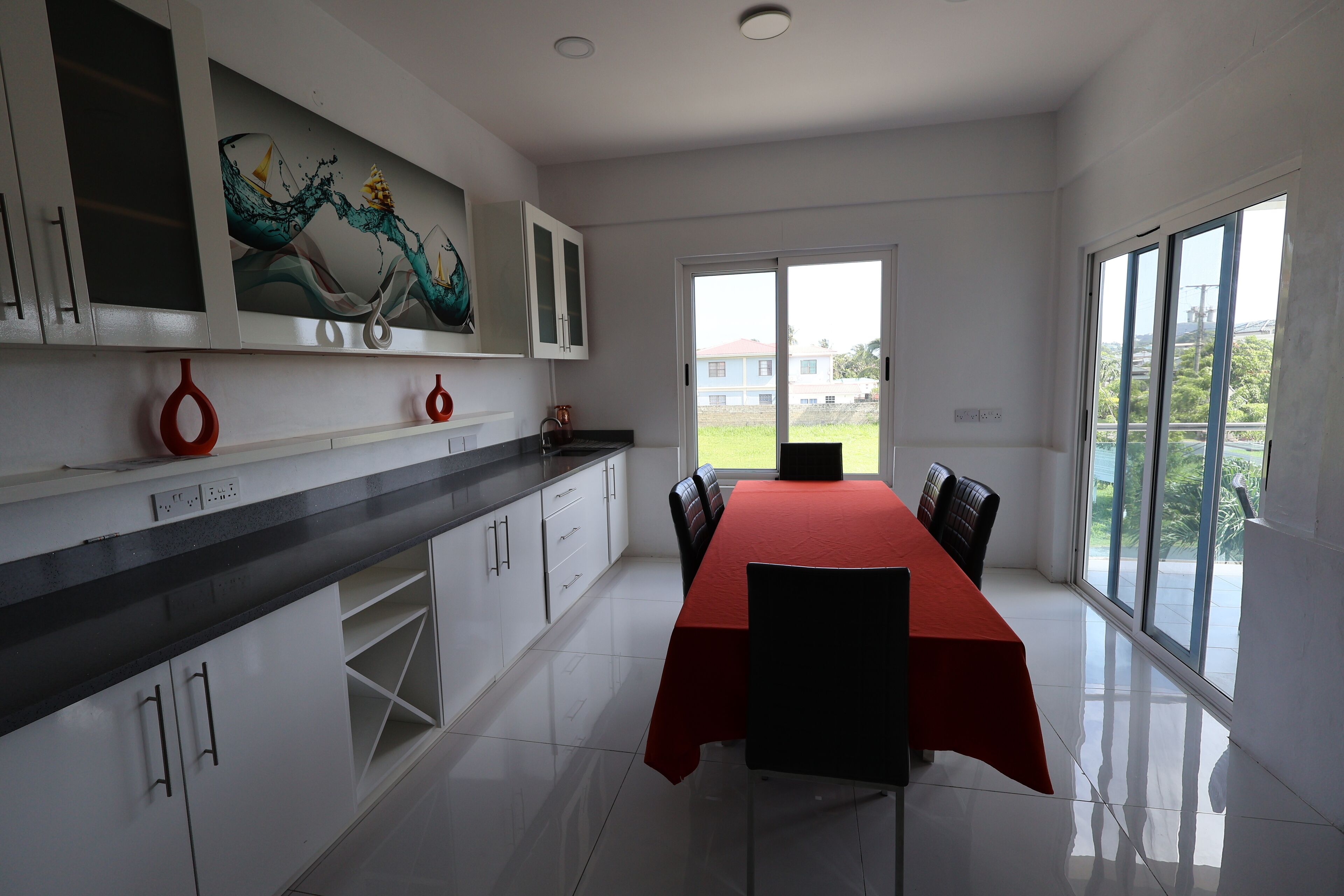 Een moderne keuken met witte kasten, een zwart aanrecht en een rode eettafel met stoelen.