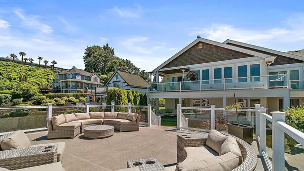 A waterfront property with a large outdoor seating area, a covered deck, and a view of the water and neighboring houses. - Cozy Old Town condo + Garage + Patio Steps to Ruston Way! (Tacoma)