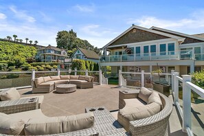 A waterfront property with a large outdoor seating area, a covered deck, and a view of the water and neighboring houses. - Cozy Old Town condo + Garage + Patio Steps to Ruston Way! (Tacoma)