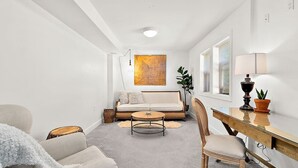 A modern living room with a sofa, coffee table, and a desk with a lamp. - Cozy Old Town condo + Garage + Patio Steps to Ruston Way! (Tacoma)
