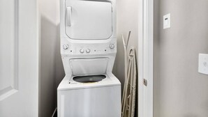 A compact, white laundry room with a built-in washer and dryer, a towel rack, and a door with a light switch. - Quiet condo Steps to Tacoma Dome~Bay & City VIEWS! (Tacoma)