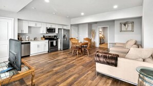 A spacious living area with a wooden floor, a sofa, a television on a glass table, and a kitchen with white cabinets and modern appliances. - Quiet condo Steps to Tacoma Dome~Bay & City VIEWS! (Tacoma)