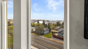 A view from a window overlooking a street with houses, a road, and a large white dome structure in the distance. - Tacoma Dome condo w Mountn & Bay views + + PRK! (Tacoma)