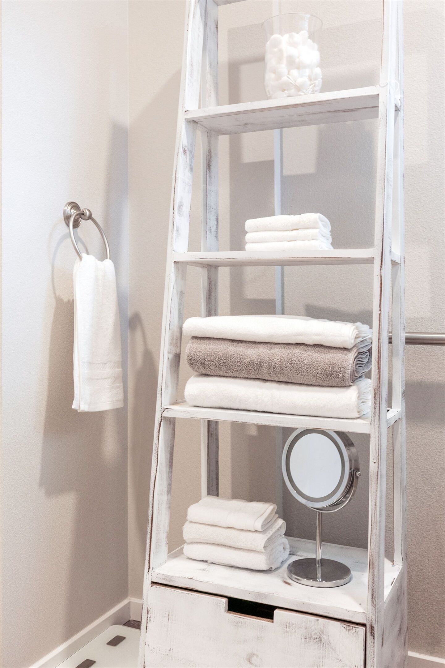 Une étagère en bois peinte en blanc, sur laquelle sont posées des serviettes, et un miroir rond.
