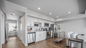 A modern kitchen with white cabinets, stainless steel appliances, and a wooden floor. - Steps to Dome Breathtaking views + parking + AC! (Tacoma)