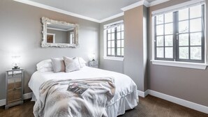 A bedroom with a large bed, a mirror, two bedside tables, and two windows.