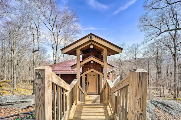 Una cabaña de madera con porche y puerta, rodeada de árboles.