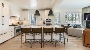 Una cocina moderna con armarios blancos, una isla central con taburetes y luminarias colgantes.