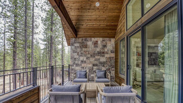 Una terraza de madera con un muro de piedra, dos sillas de mimbre y una mesa.