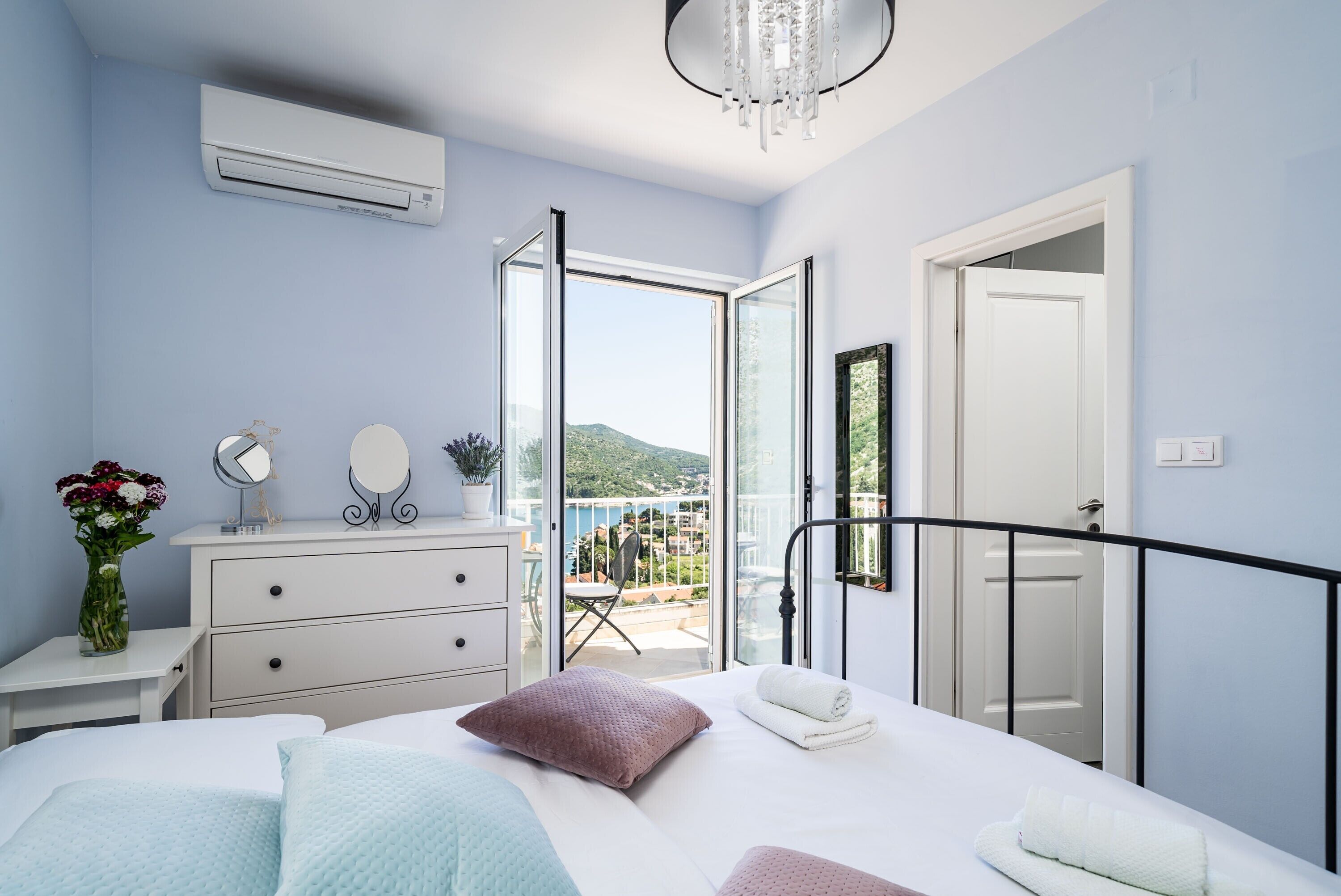A bedroom with a bed, bedside tables, a dresser, a mirror, and a view of a balcony with a chair and table.