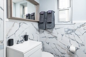 Ein Badezimmer mit Marmorwänden, einem weißen Waschbecken, einem Spiegel und zwei an der Wand hängenden Handtüchern.
