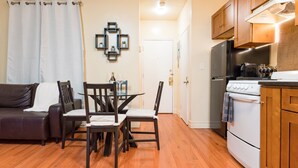 Un espacio habitable compacto con comedor, sofá, cocina con refrigerador y estufa, y una puerta que da a otra habitación.