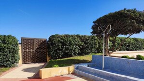 Un espace piscine doté d’une terrasse carrelée de carreaux bleus, d’une pergola en métal et d’un mur en briques.