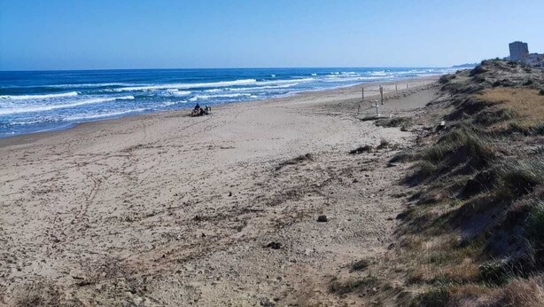 Une plage avec un ciel dégagé, un rivage sablonneux et quelques personnes.