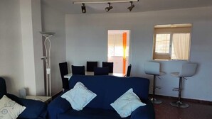 Un salon avec un canapé bleu, une table blanche et un coin repas avec des chaises.